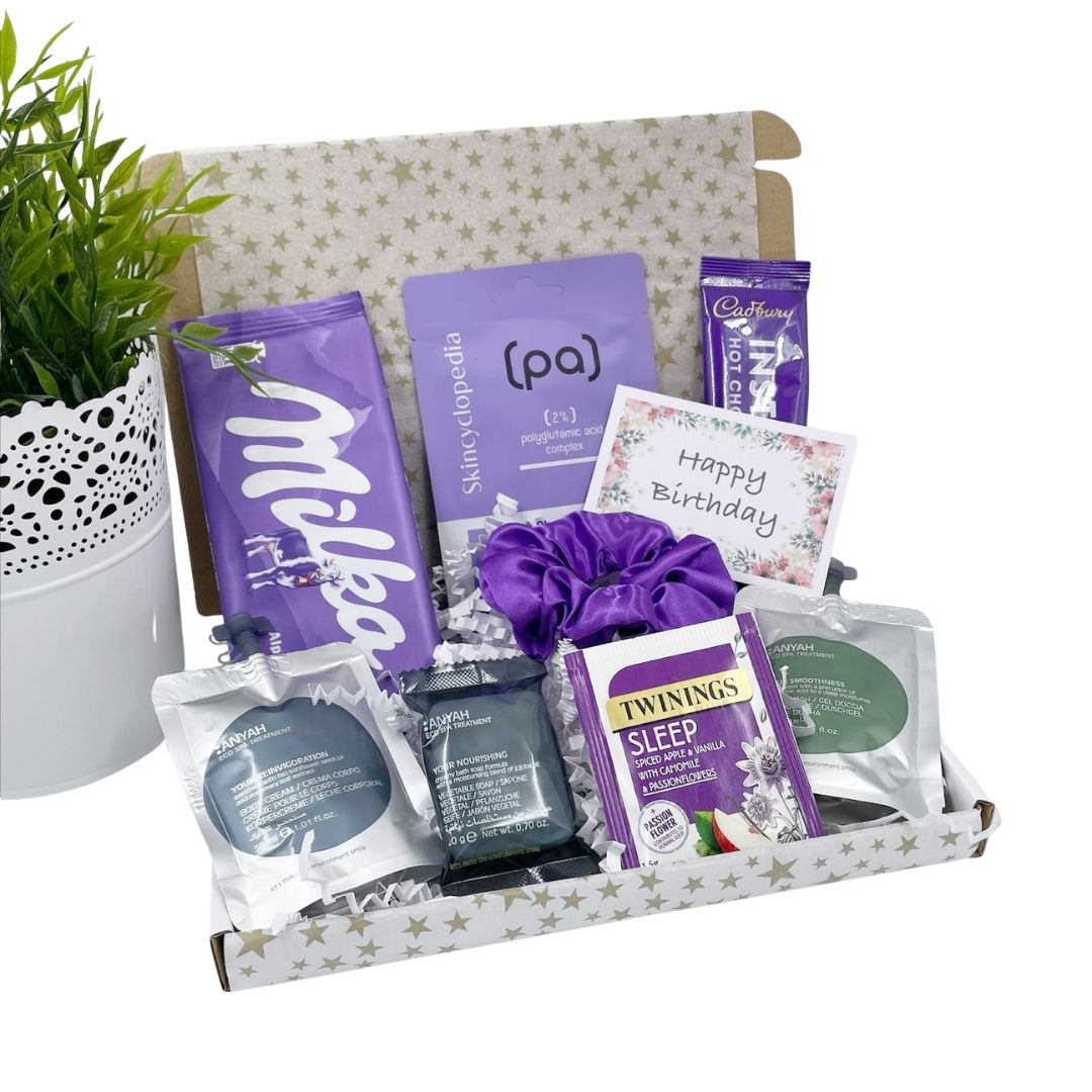 Gift basket with various items including a plant, purple chocolate bars, and tea packages on a white background.