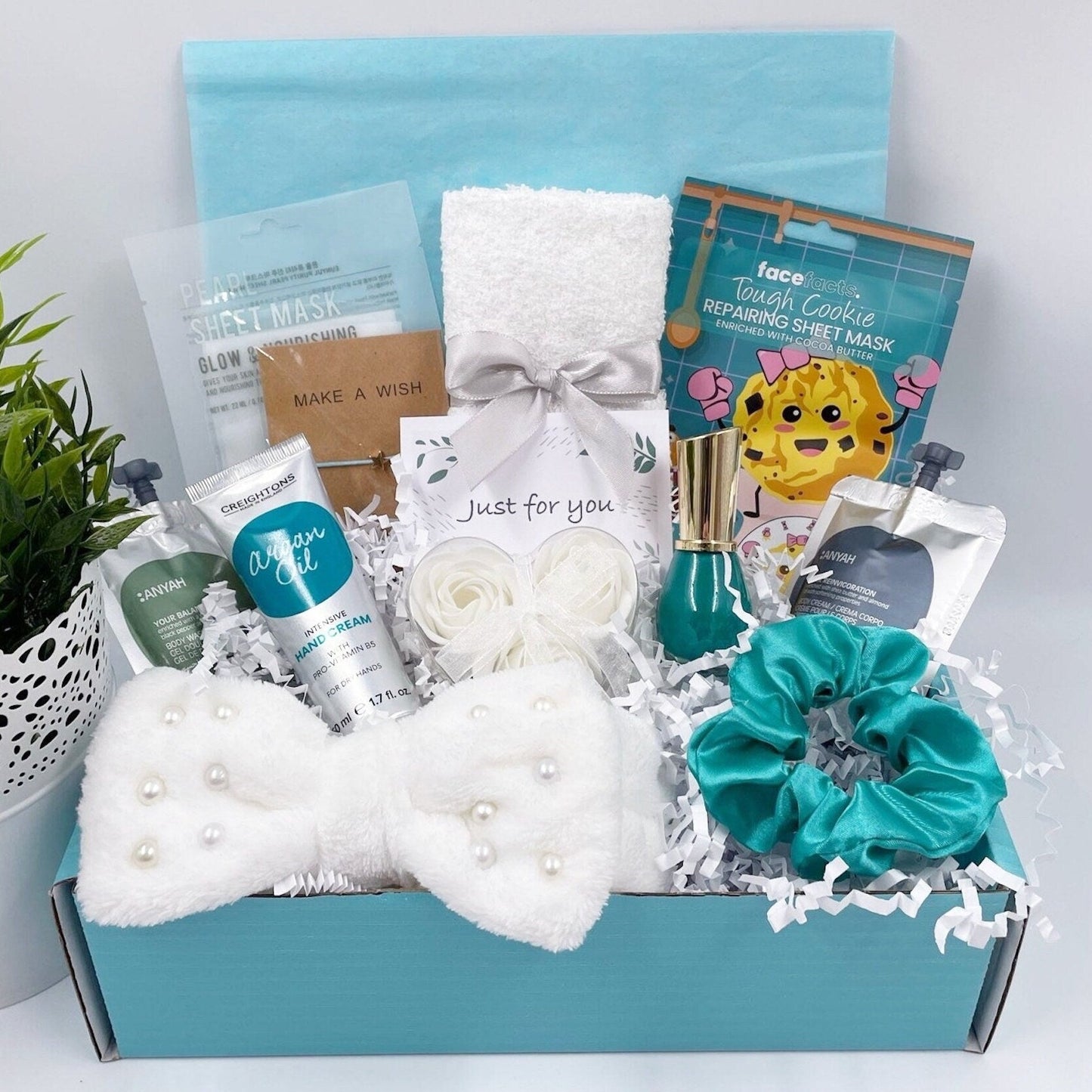 A gift box containing various spa-related items such as a face mask, nail polish, body wash, body lotion, rose flower soaps, a bracelet, hair accessories, a face towel, and hand cream, all packaged in a decorative teal box.