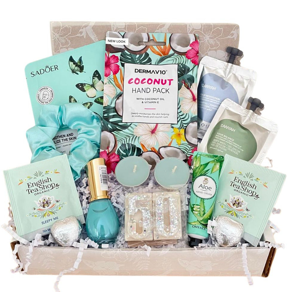 A curated self-care gift box filled with multiple beauty products including Dermvav10 Coconut Hand Pack, Sadoer  sheet mask, English Tea Shops tea bags, a teal nail polish, glittery wax melts, wrapped chocolates, satin scrunchie, Handcream scented candles in a box with fancy tissue and gift card of your choice.